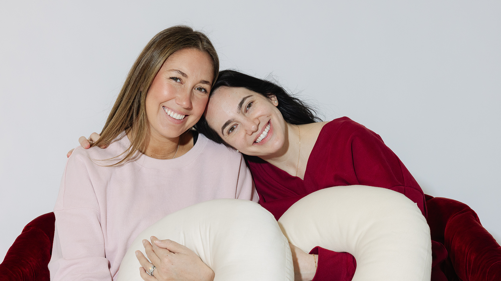 Two women sitting together, each is holding a white tush present pillow 