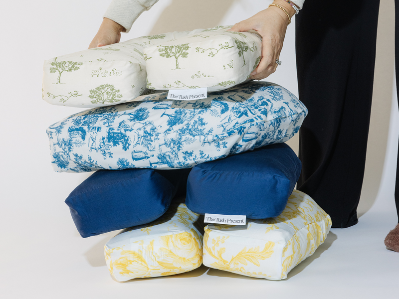 Stack of patterned tush pillows with visible brand labels on a white background